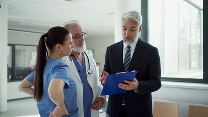 Medical sales representative presenting new medication to doctors, standing hospital hallway.
