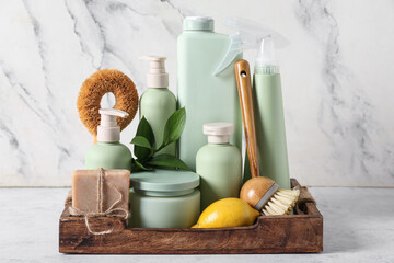 Tray with set of natural cleaning supplies on table near white marble wall