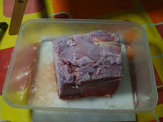 Frozen raw red meat, beef is seen in a clear plastic container, ready to be stored or thawed for...