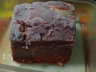 Frozen raw red meat, beef is seen in a clear plastic container, ready to be stored or thawed for...