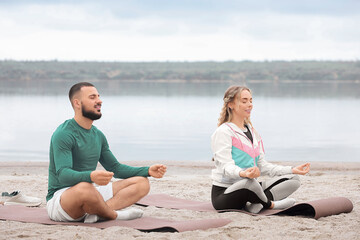 Sporty young couple meditating on river bank