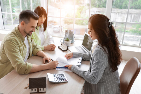 Female Asian real estate agent with couple signing agreement in office