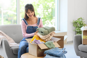 Young woman packing clothes into box for donation at home
