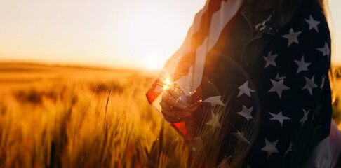 Close-up Young woman with American flag holding fireworks sparklers in a wheat field at sunset. 4th...