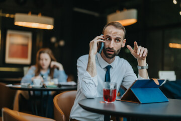 Obraz premium A professional businessman having a phone conversation in a modern coffee shop atmosphere. His tablet and a cup of tea are on the table as he actively engages in communication.