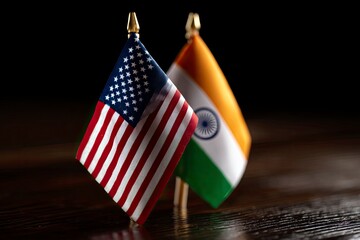 Two miniature flags one US and one India stand on a polished wooden surface Dark background