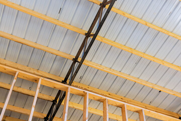 Fototapeta premium Wooden beams metal supports are visible during construction of building with sheet metal roof.