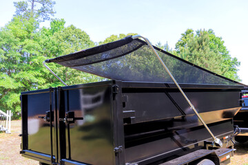 Black utility container trailer features tarpaulin cover in sunny environment
