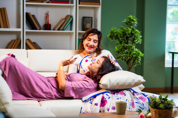 Daughter sleeping on mother’s lap while seated on sofa at home in warm emotional bonding scene