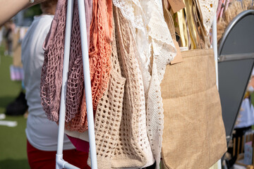 A beige and natural colors display of crochet bags in diverse patterns hangs neatly at a market stall. Lively and inviting shopping scene at outdoor market.