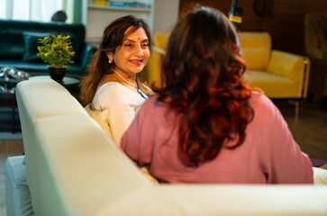 Indian mother and daughter relaxing on sofa and talking over hot coffee in cozy modern home
