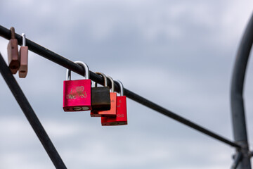 Close-up red love-lock with "I love you" inscription, hanging on iron structure, sky blurred. Symbol of love, passion, relationship