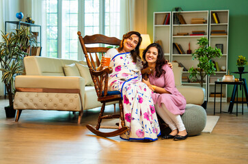 Indian woman serving orange juice to old mother in saree sitting on rocking chair at home