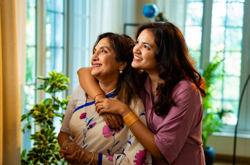 Indian mother daughter enjoy morning tea by window while smiling and bonding peacefully at home