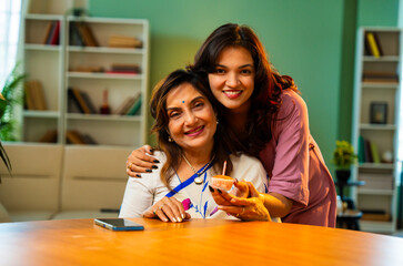 Daughter surprises Indian mom with birthday cake, candle, and hug in cozy home setting