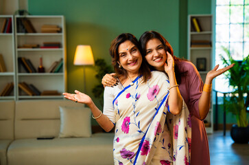 Smiling Indian mother and daughter looking at camera indoors with positive expressions