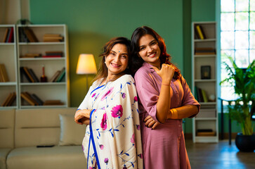 Smiling Indian mother and daughter looking at camera indoors with positive expressions