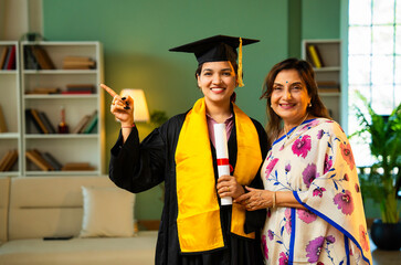 Indian Female graduate in gown shows degree to mother and hugs happily during home celebration