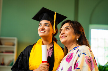 Indian Female graduate in gown shows degree to mother and hugs happily during home celebration