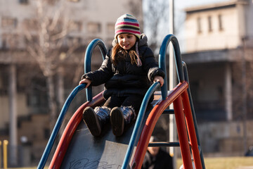 Naklejka premium Happy child sliding down playground slide in winter clothes