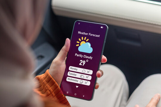 A Muslim woman in a car checking the weather forecast using an app on her smartphone