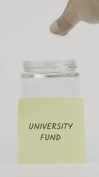 University fund text or word on a yellow sticky note attached to a glass jar. A hand inserts a coin, symbolizing hidden goals or confidential savings. White background, vertical screen