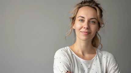 A beautiful young woman with blonde hair and blue eyes is smiling at the camera. She is wearing a white shirt with black polka dots.