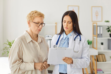 Young doctor woman holding report file with appointment and prescribe treatment to female mature...