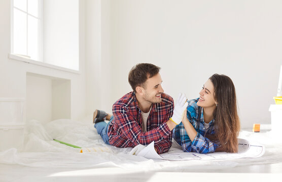 Husband and wife collaborate on planning a renovation project at home, reviewing blueprints and exchanging a high five. Couple teamwork demonstrates dedication to the shared construction task.