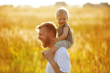 Happy father carries his little son on his shoulders.
