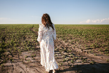 Young woman walking away in cultivated field during summer sunset