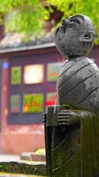 An ancient stone figure facing an artificial waterfall, Huanglongxi Ancient Town, Chengdu, Sichuan, China