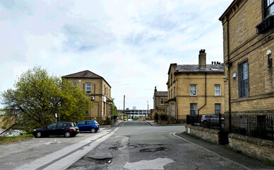 A street scene with Victorian Stone buildings and a few parked cars along the side of the road. The...