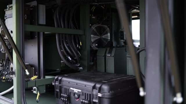 Interior of military command vehicle filled with cables power units control modules and a rugged black case showing technical core of mobile field operations and communications hub