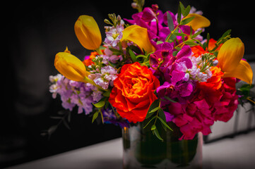 Vibrant flower bouquet with red carnation and yellow tulips and pink and purple flowers on the table against the monotone black background