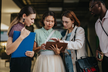 A group of diverse international business people engaged in a discussion using a tablet in an urban city environment, showcasing teamwork and collaboration.