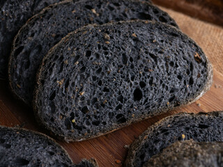 Fresh baked black charcoal sourdough ciabatta bread sliced on wooden board.