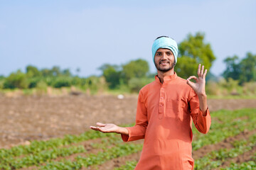 young indian farmer standing at green agricultural field