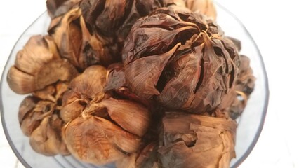 Top-down shot of glossy black garlic bulbs in a clear glass bowl against a white background...