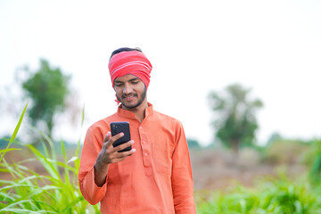 young indian farmer using smartphone standing at agricultural field