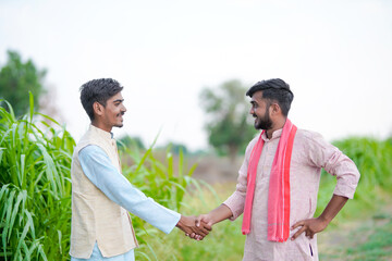 young indian farmer shaking hand together at agricultural field