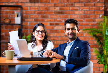 Indian businessmen Working on laptop and reviewing project papers together at desk in indoor office