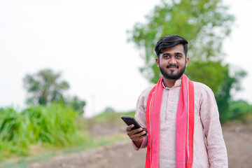 young indian farmer using smartphone standing at agricultural field