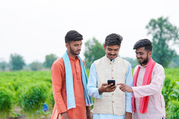 three young indian farmer holding smartphone together at agricultural field