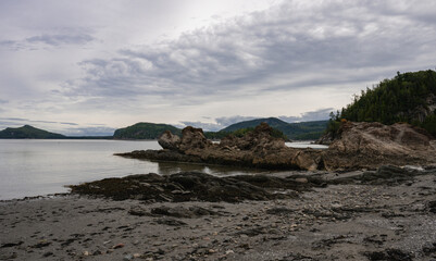 low point of view from the rocky beach of a lake shore with a calm lake under a soft cloudy sky  in summer 