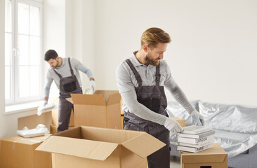 Movers male team packing, choosing cardboard box, arranging items carefully inside, preparing for...