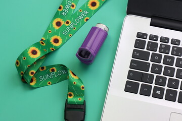 Hidden disability lanyard with a asthma device close to a laptop in a green background