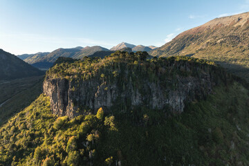 Cliff face with columnar basalt formations under blue sky framed by Araucaria trees. Neuquen, Patagonia, Argentina