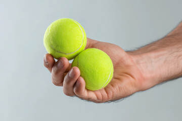 male hand holding two tennis balls, representing testicles and masculinity isolated on plain gray background