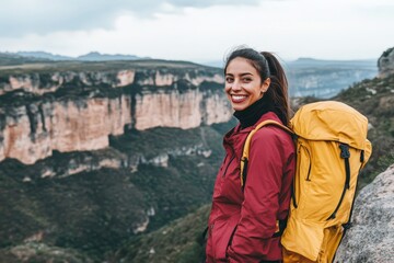 Naklejka premium Smiling woman with a backpack stands on a mountaintop overlooking a canyon.